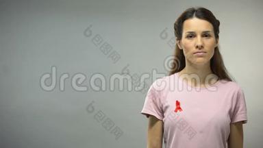 穿着红色缎带的年轻女子在镜头前看着艾滋病毒/艾滋病宣传标志